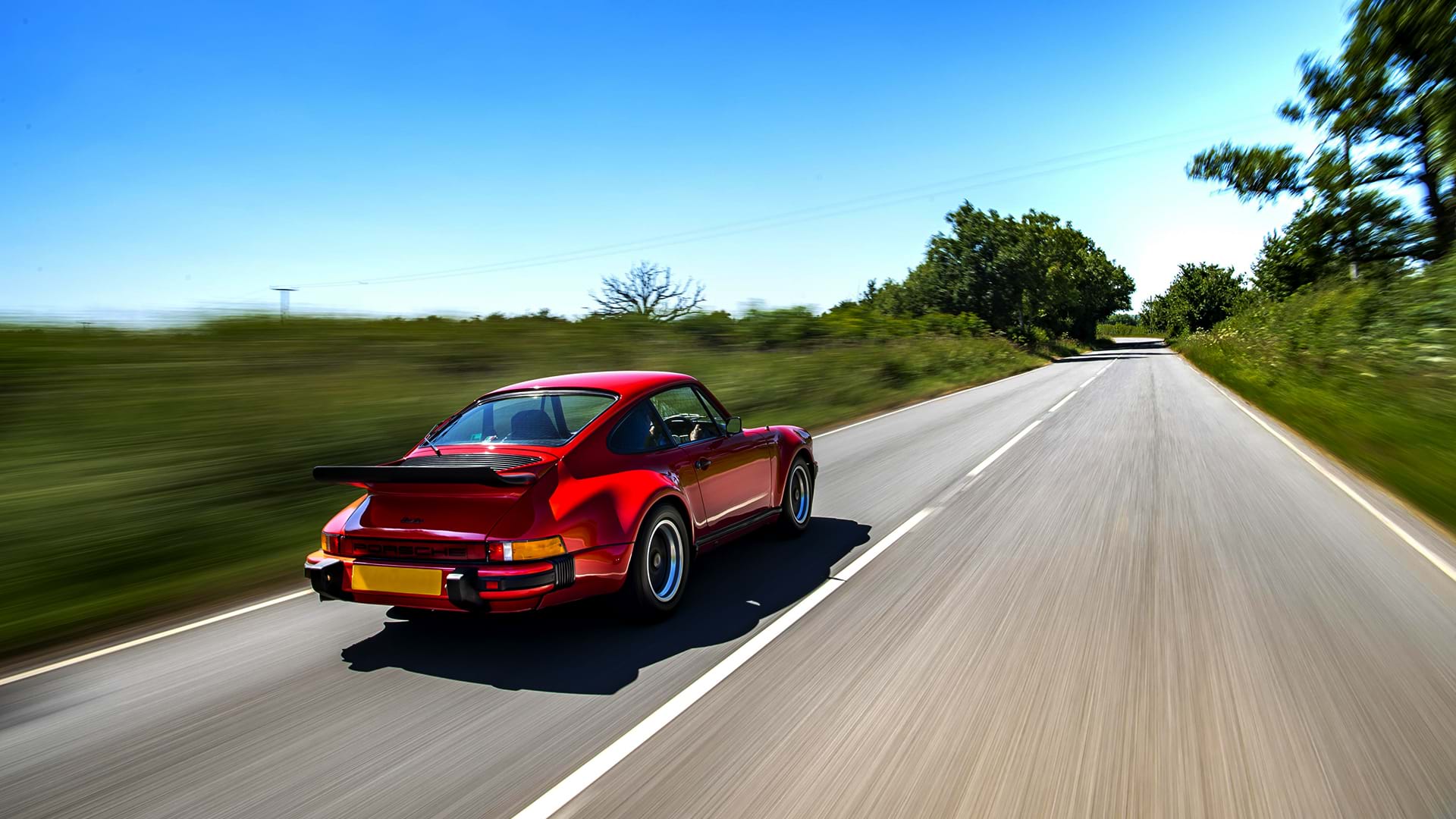 Vintage red Porsche 930 Turbo roaring down a beautiful country road on a sunny day.